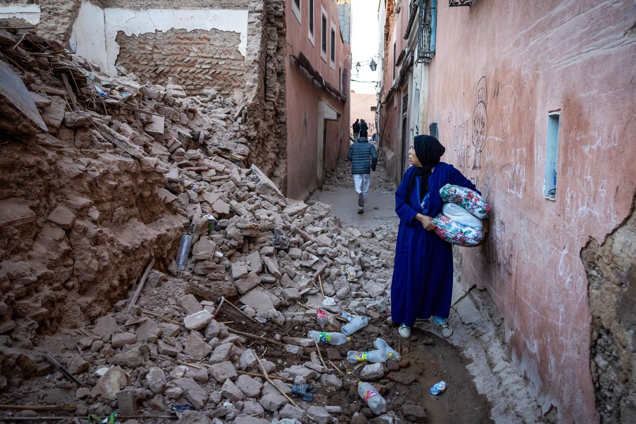A woman looks at the rubble of a building.