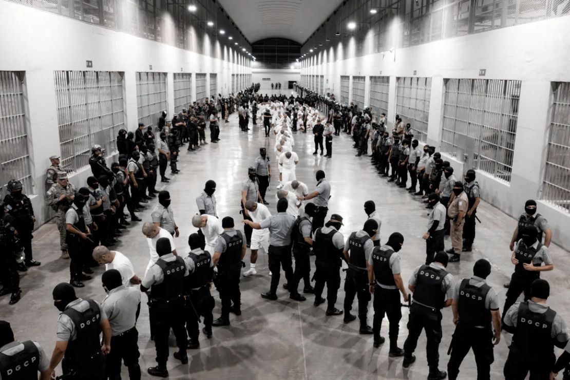 En esta fotografía obtenida el 16 de marzo de la Oficina de Prensa de la Presidencia de El Salvador, agentes de la Policía salvadoreños escoltan a venezolanos recientemente deportados por el Gobierno de Estados Unidos en la prisión del Centro de Reclusión del Terrorismo en Tecoluca, El Salvador.