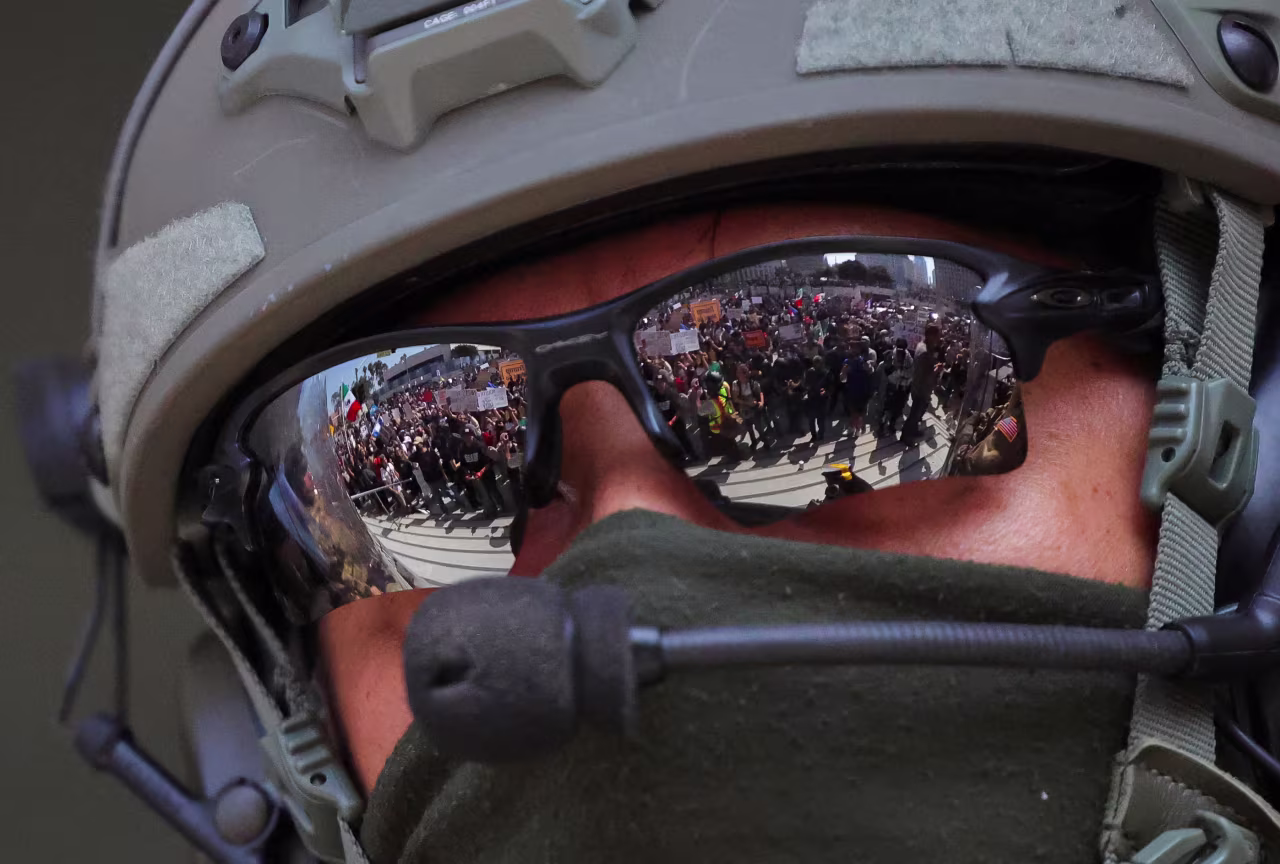Protesters are reflected in the sunglasses worn by a law enforcement officer.