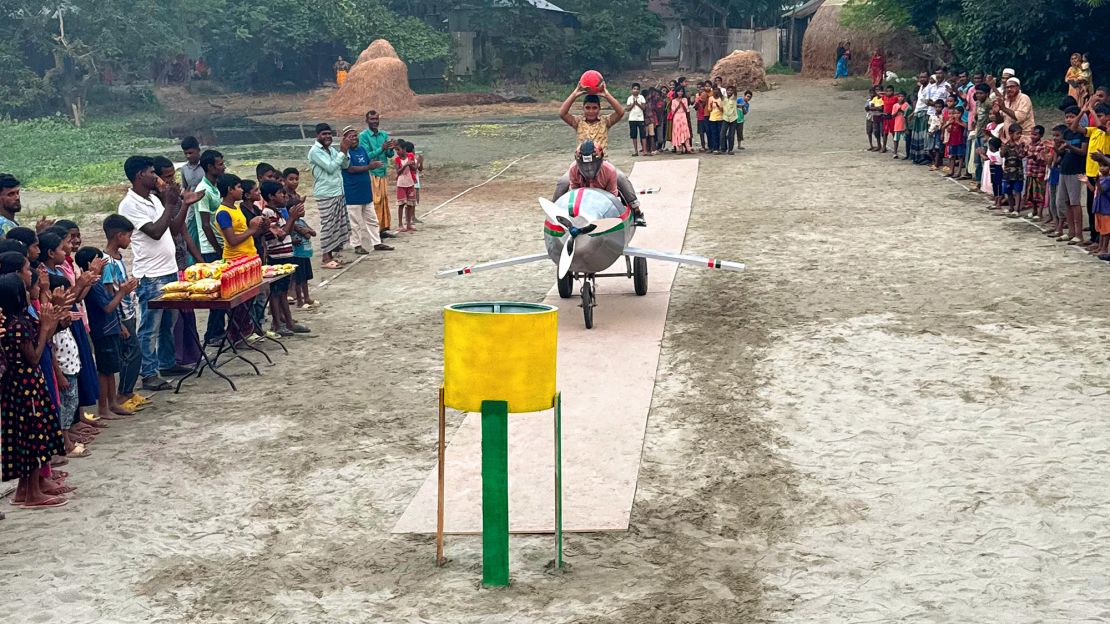 A player glides down a makeshift jet on cardboard runway, holding a ball and aiming for the basket during a game in Purandarpur village in the Pabna District of Bangladesh on October 17, 2023.