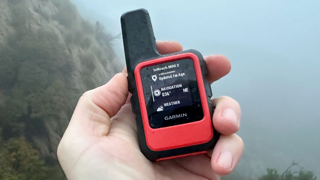 The Garmin inReach Mini 2 is held in a left hand with a foggy view in the background.