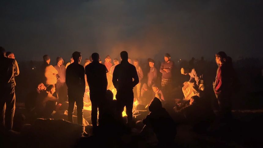 Thousands of people wait overnight for aid trucks to pass. Only a few women can be spotted among the crowds.