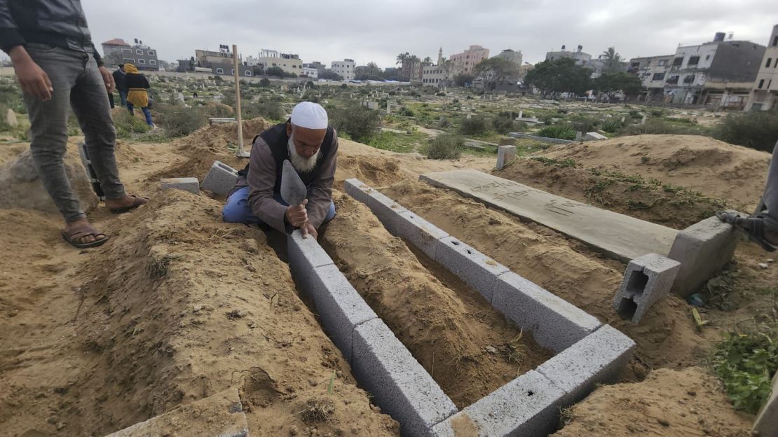 Baraka lays concrete bricks to form the walls of a grave above ground.