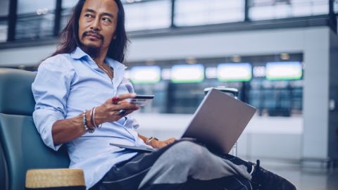 Man using laptop and a credit card while waiting at the airport terminal.