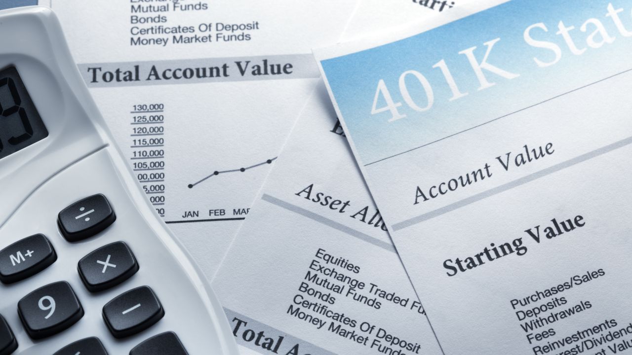 A calculator rests on top of the pages of a 401K retirement account statement.