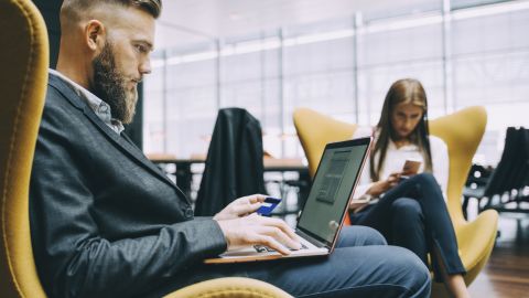  A man in a suit looking at a laptop and a credit card.