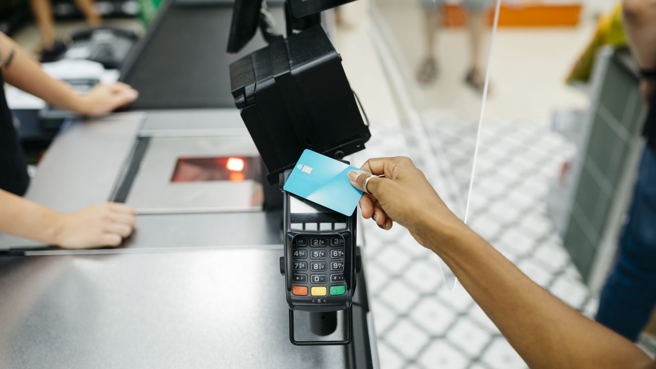 Hand tapping a blue credit card on a payment terminal