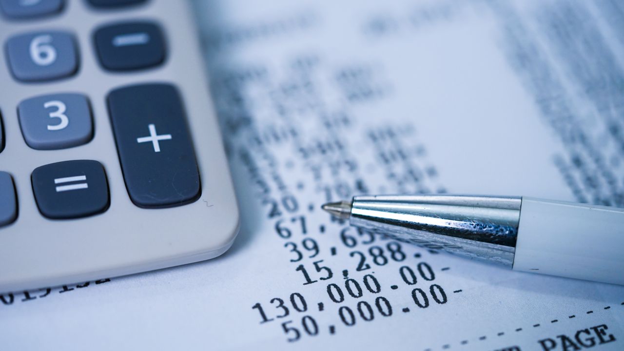 A calculator and a pen on top of a piece of paper with number amounts on it.