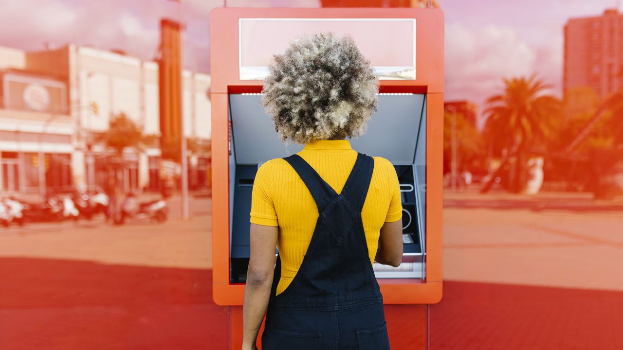 Person, die einen leuchtend roten Geldautomaten benutzt.