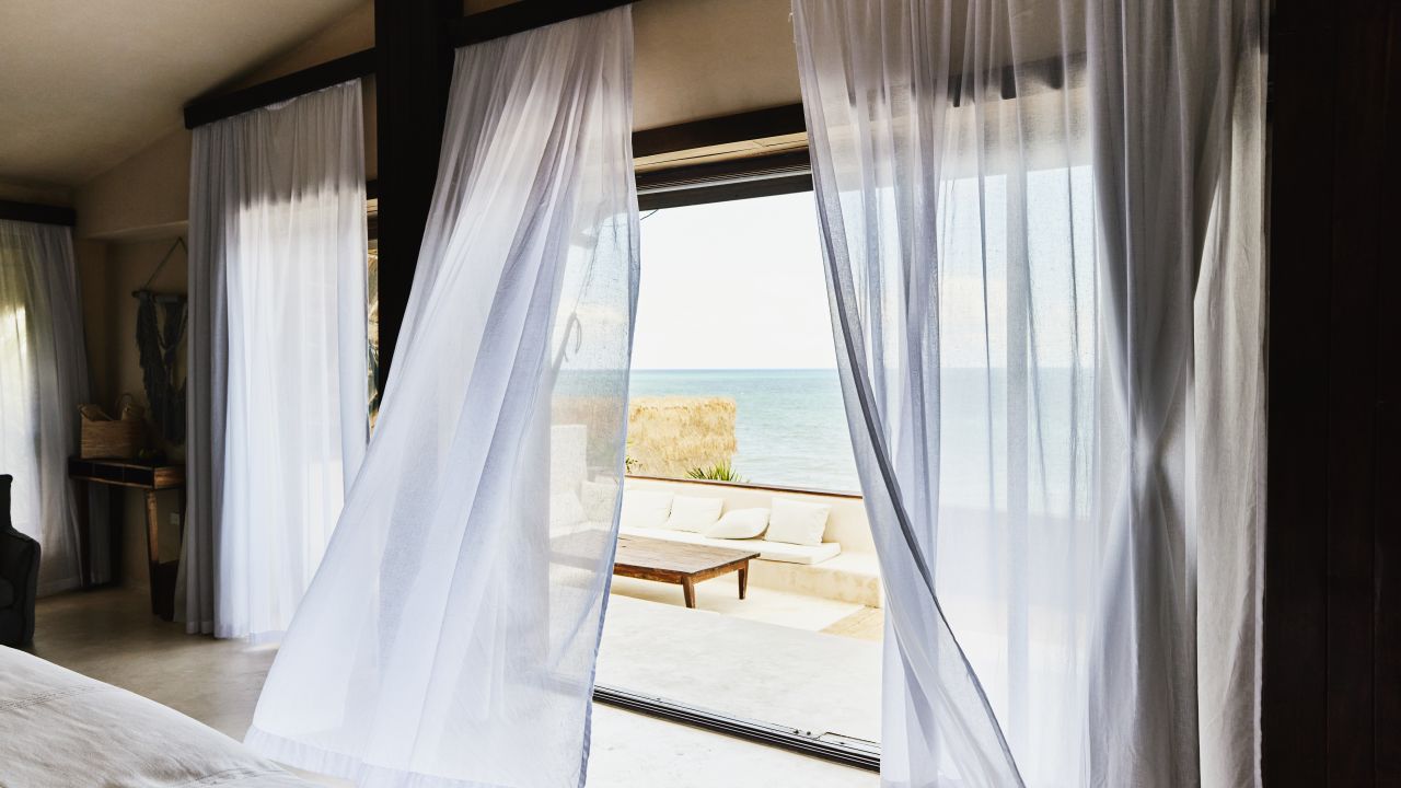 Wide shot of curtains blowing in wind in luxury suite at tropical resort.