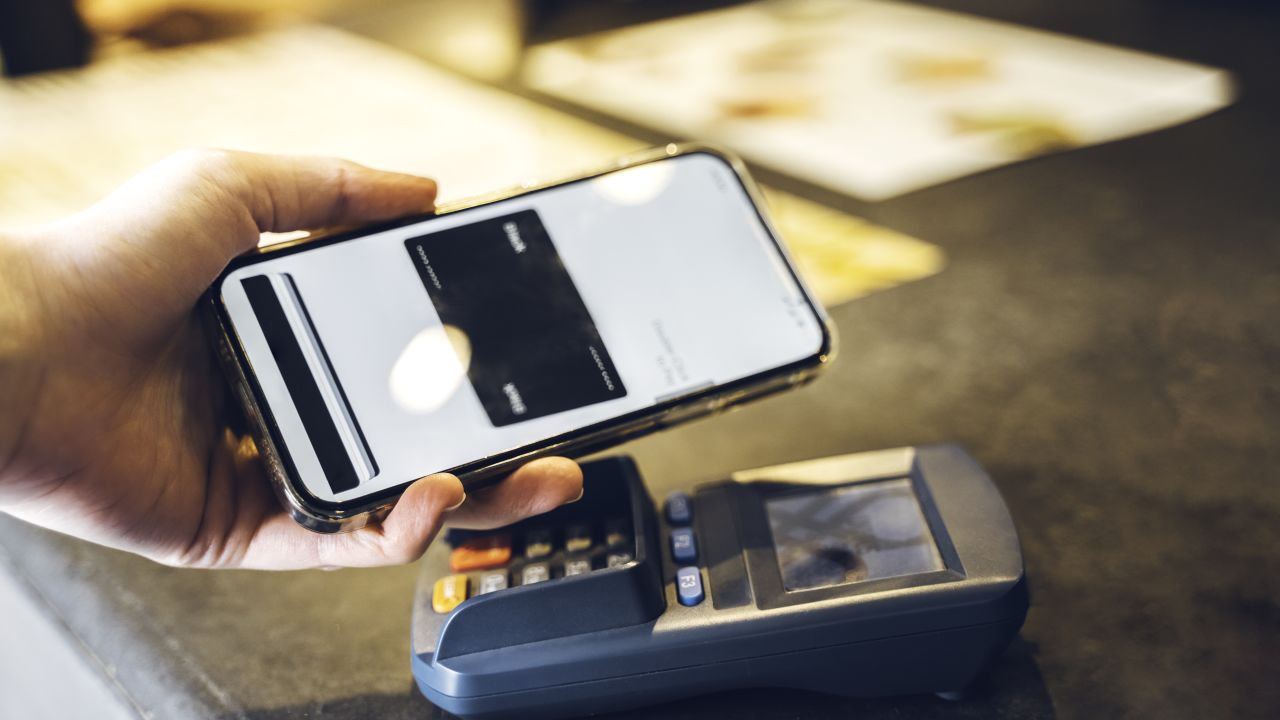 Hand tapping a smartphone over a contactless credit card reader.
