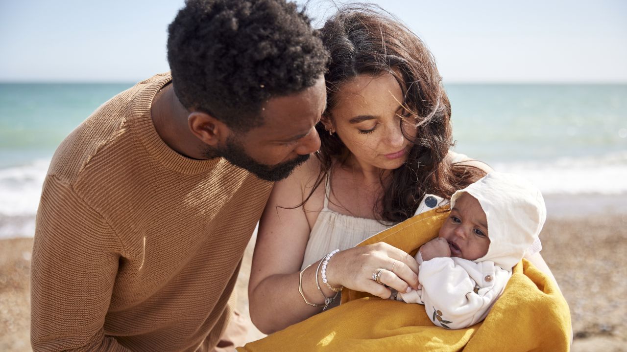 Sepasang suami isteri menggendong bayi di pantai.