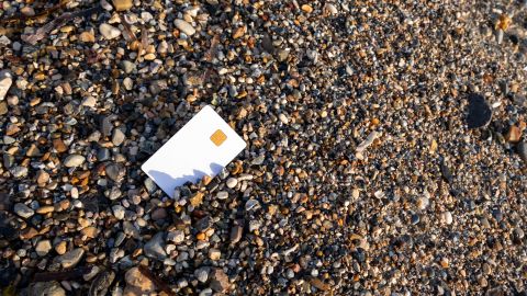 A blank credit card lies on sand and pebble beach in Greece