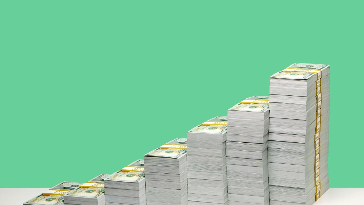 Stacks of $100 bill bundles in ascending order on a green background