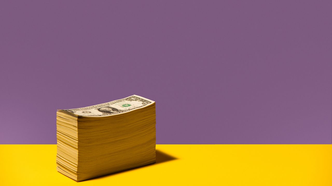 A stack of $1 bills on a purple and yellow background.