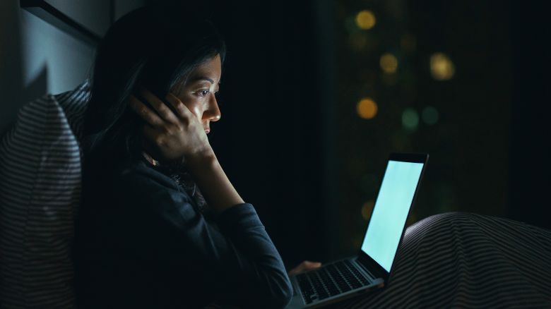 Young woman in deep thought while using laptop on bed at night