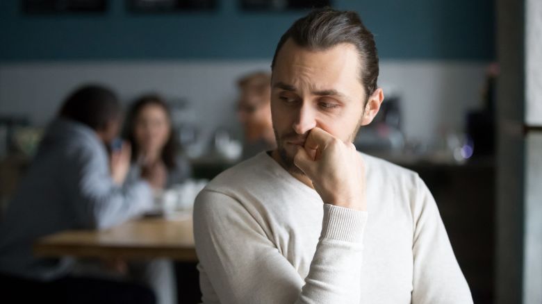 Upset millennial outsider feel offended lack company, young outcast guy suffer from discrimination, jealous of friends hang out together in cafÃ©, envious male loner depressed sit alone in coffeeshop