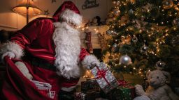 Santa Claus putting gifts under the christmas tree at night