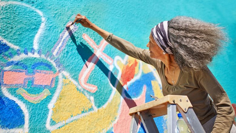 Senior woman painting vibrant mural on sunny wall