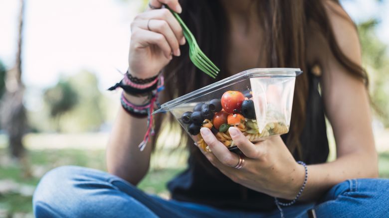 Young woman sitting in a park, eating salad