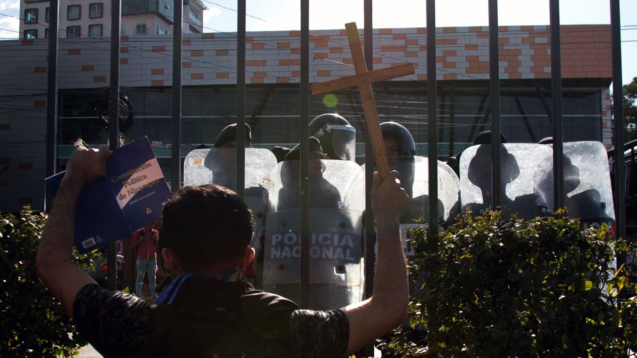 An opposition protester shows the Nicaraguan Constitution to riot police from a shopping mall where he and others took refuge after they were prevented by the police from demonstrating against the government to demand the release of those arrested for taking part in anti-government protests, in the surroundings of the Centroamerica roundabout in Managua on March 16, 2019. - Nicaragua on Friday released 50 prisoners held for participating in anti-government protests, giving a fresh impetus to peace talks on ending the country's long running political crisis. More than 700 people were detained during a deadly crackdown on rallies that began last April and quickly grew into broad opposition to President Daniel Ortega iron-fisted rule. (Photo by Maynor Valenzuela / AFP)        (Photo credit should read MAYNOR VALENZUELA/AFP via Getty Images)