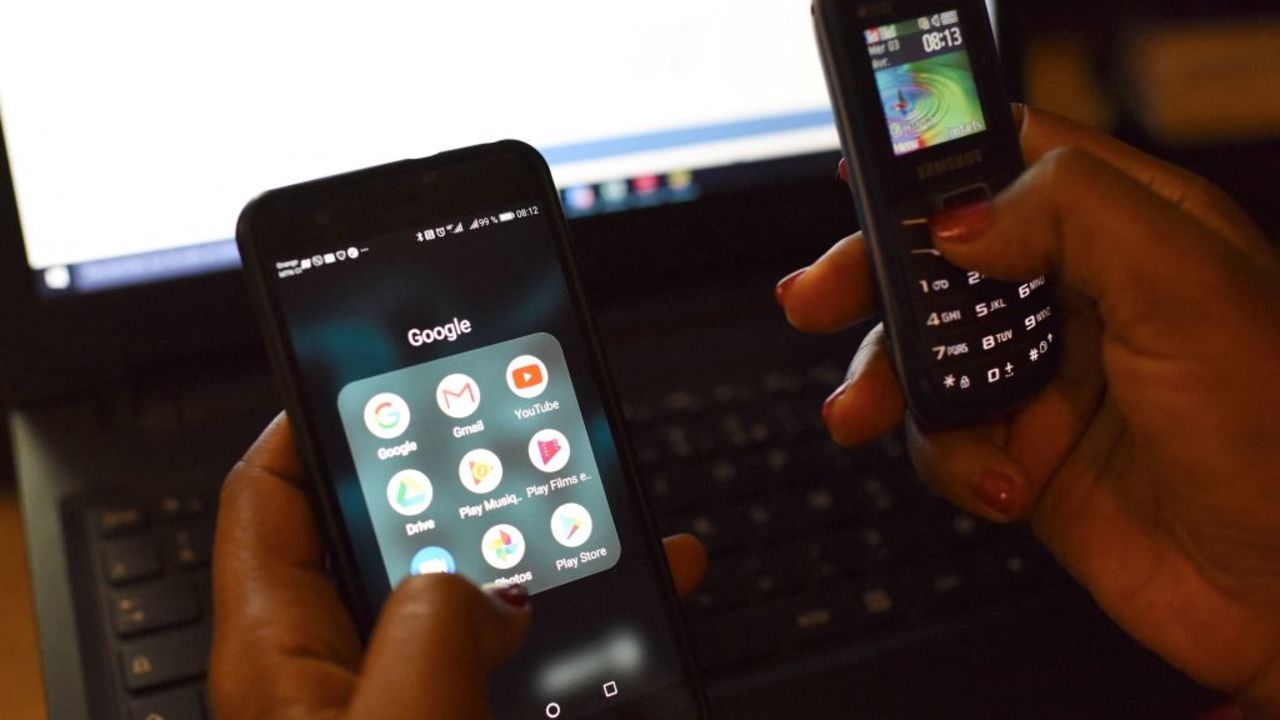 A woman uses a smartphone and a mobilephone in front of a laptop on April 3, 2019, in Abidjan. - According to the figures of the platform of the fight against cybercrime (PLCC) of the national police, nearly one hundred crooks of the internet, were arrested in 2018 in Ivory Coast, a country known for its scammers on the web, has announced on April 2, 2019 the Ivorian authority of regulation of the telephony. (Photo by ISSOUF SANOGO / AFP) (Photo by ISSOUF SANOGO/AFP via Getty Images)