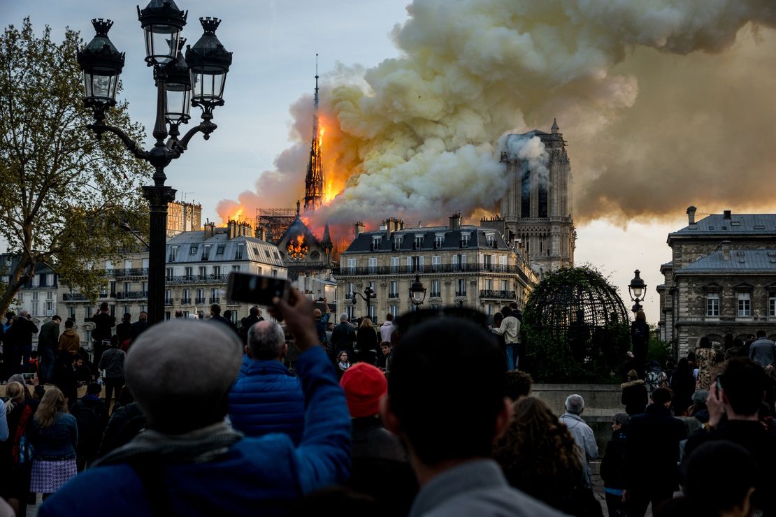People watch the landmark Notre-Dame Cathedral burning in central Paris on April 15, 2019- Investigations were not able to pinpoint the exact cause of the fire. 