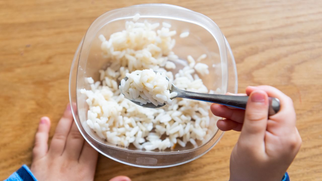 child hand holding a fork, he is having rice, from above