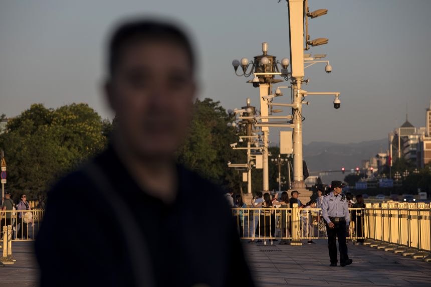 A police officer walks past a surveillance camera installed on a pillar in Tiananmen Square in Beijing on May 31, 2019.