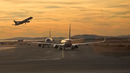 A jet takes off as another comes in for a landing and two jets wait on the runway.
