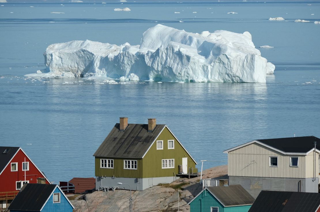 An iceberg floats past houses on Disko Bay, Greenland, during unseasonably warm weather on July 30, 2019.