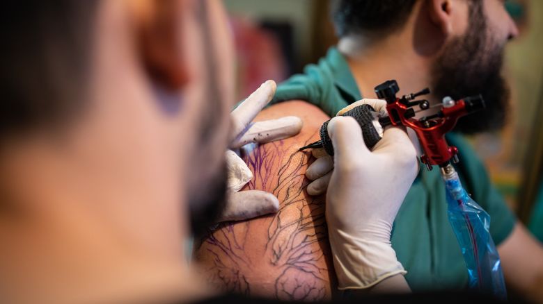 Close up of tattoo gun while artist painting tattoo on human's arm