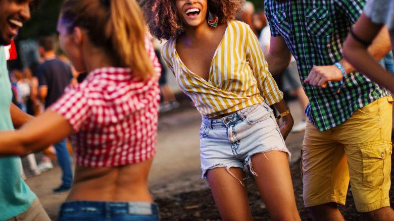 Friends dancing and jumping at music festival. Young african american woman laughing, jumping and looking at camera.