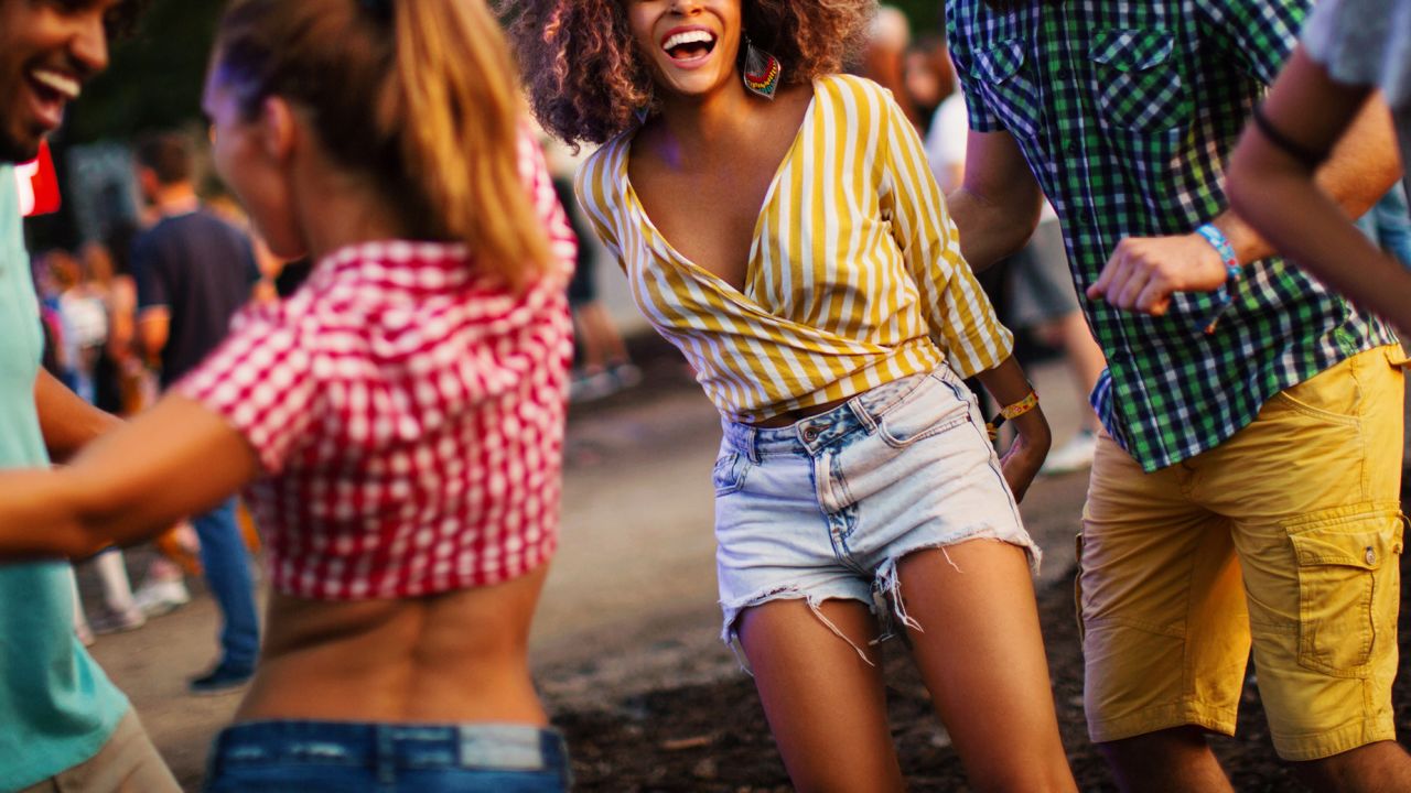 Friends dancing and jumping at music festival. Young african american woman laughing, jumping and looking at camera.