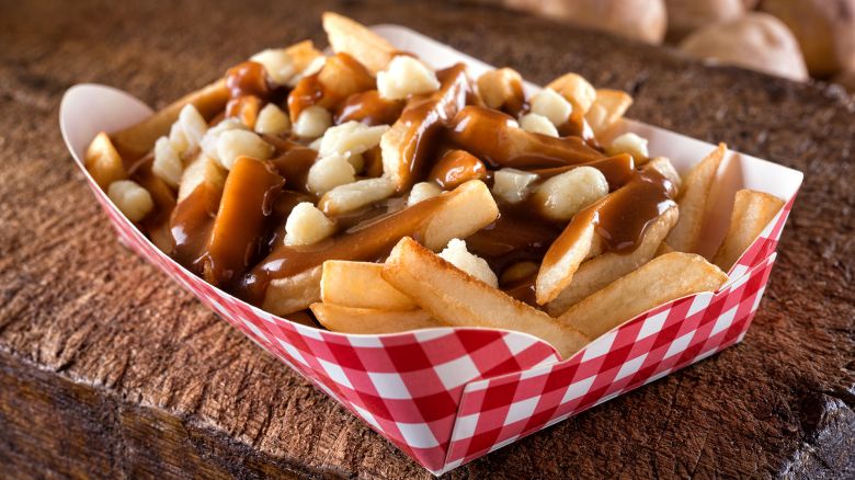 A serving of delicious poutine with french fries, cheese curds and gravy on a rustic wooden board.