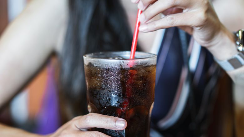 woman hand drinking glass of cola with ice, unhealthy lifestyle concept