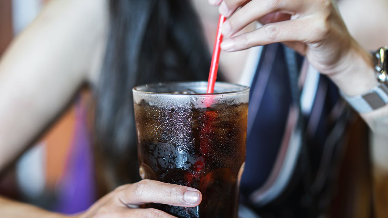 woman hand drinking glass of cola with ice, unhealthy lifestyle concept
