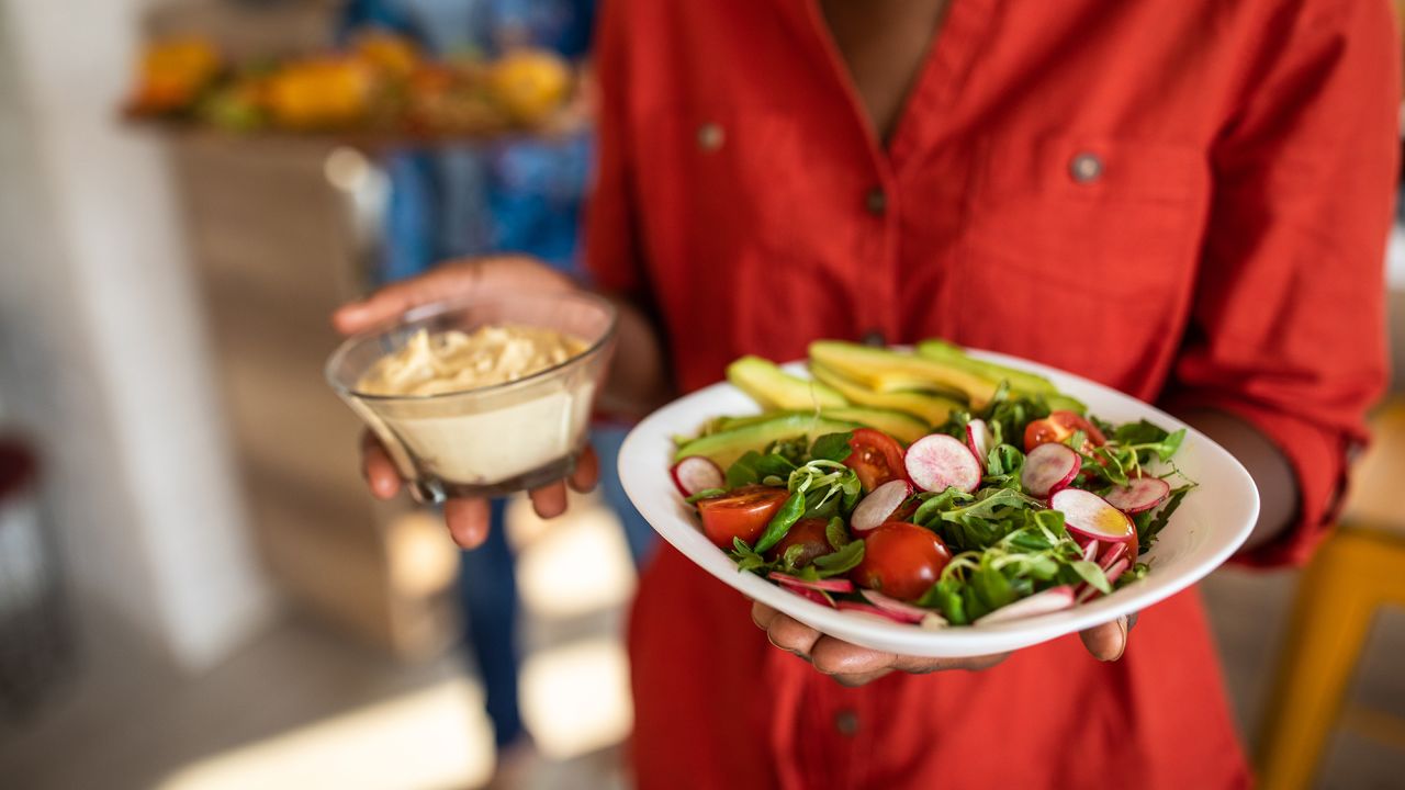 Unrecognizable  woman serving vegetarian meal to friends at home on  plate
