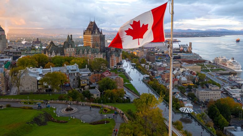 A flowing Canadian flag on a flagpole. Taken at sunset with Old Quebec City and the St. Lawrence River in the background. Aerial HDR view.