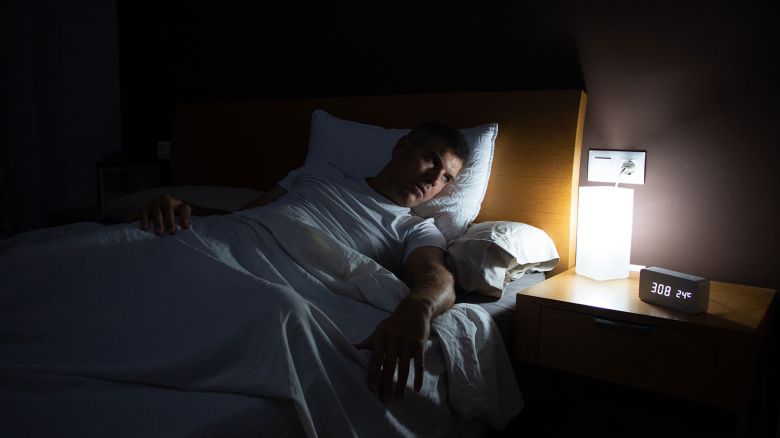 A man with insomnia looks at the clock at dawn from the bed with concern. Lifestyle concept
