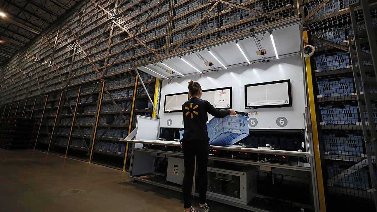 A Walmart employee loads up the Alphabot with an empty cart to be filled with a customer's online order at a Walmart micro-fulfillment center in Salem, MA on Jan. 8, 2020. Walmart has teamed up with Alert Innovation, a robotics engineering team firm in North Billerica, to build the 20,000-square-foot, semi-automated miniature warehouse next to a Walmart Superstore. Humans and robots work together to quickly pack thousands of grocery items that were ordered online from massive shelves. Each robot has geared wheels that let it climb up or down through horizontal shafts. When it reaches the right level, the robot rolls up to the correct bin, plucks it from the shelf, then descends to a packing station. The robot passes the bin to a Walmart worker who picks out the correct item and plops it into a different bin lined with standard grocery bags.