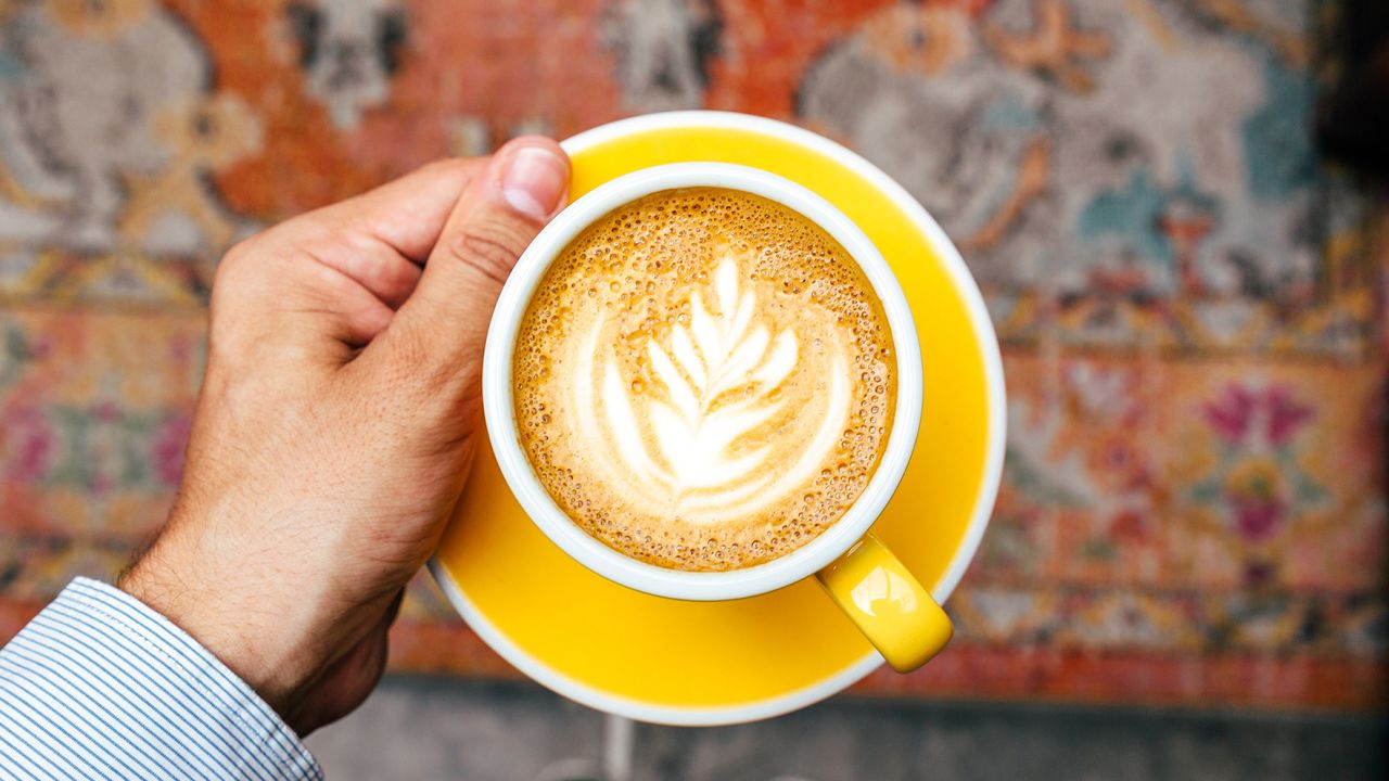 Man holding yellow cup with cappuccino, personal perspective view