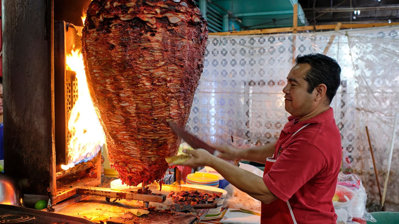 A server cuts from a large spit of meat that's roasting in a food stand in the municipal market in Mérida, Mexico.
