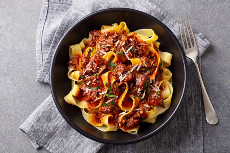Pasta pappardelle with beef ragout sauce in black bowl. Grey background. Top view.