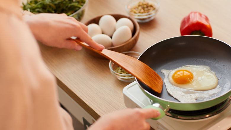 Woman cooking eggs on frying pan while preparing healthy breakfast