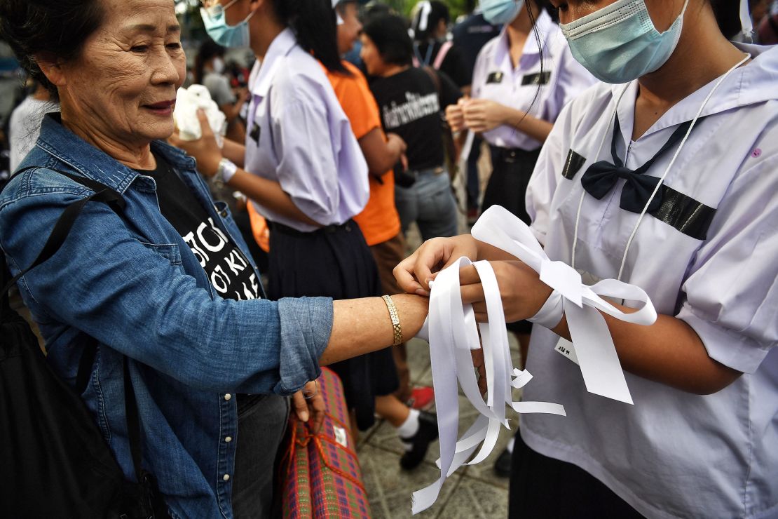 A high school student wraps a ribbon around the wrist of an elderly protester during a demonstration for educational reform and against Thailand's military government in Bangkok on September 5, 2020.