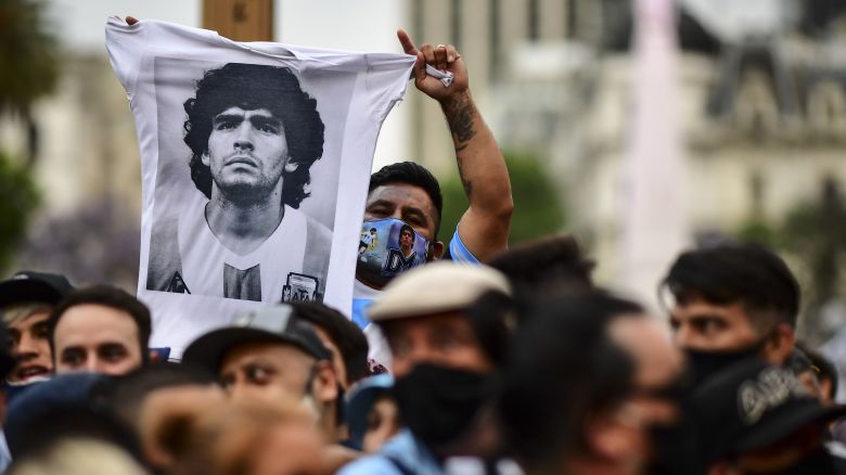 TOPSHOT - A man waves a jersey with a picture of Diego Maradona as fans wait to enter the Government House to pay tribute to late football legend Diego Armando Maradona in Buenos Aires, on November 26, 2020. - Diego Maradona's coffin arrived at the presidential palace in Buenos Aires for a period of lying in state, TV reports showed, following the death of the Argentine football legend aged 60 on November 25. Hundreds of people were already lining up to pay their respects to Maradona, who died while recovering from a brain operation, the images from sports channels TyC and ESPN showed. (Photo by RONALDO SCHEMIDT / AFP) (Photo by RONALDO SCHEMIDT/AFP via Getty Images)
