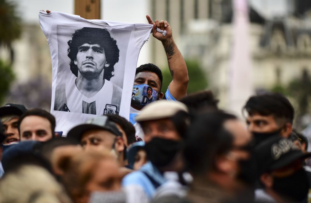 A man waves a shirt with a picture of Diego Maradona as fans wait to pay tribute to the soccer legend in Buenos Aires on November 26, 2020.