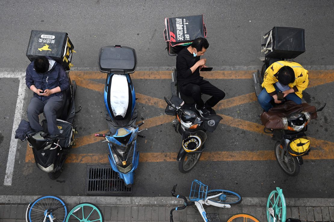 Food delivery riders wait for assignments outside a restaurant in Beijing on May 18, 2021.