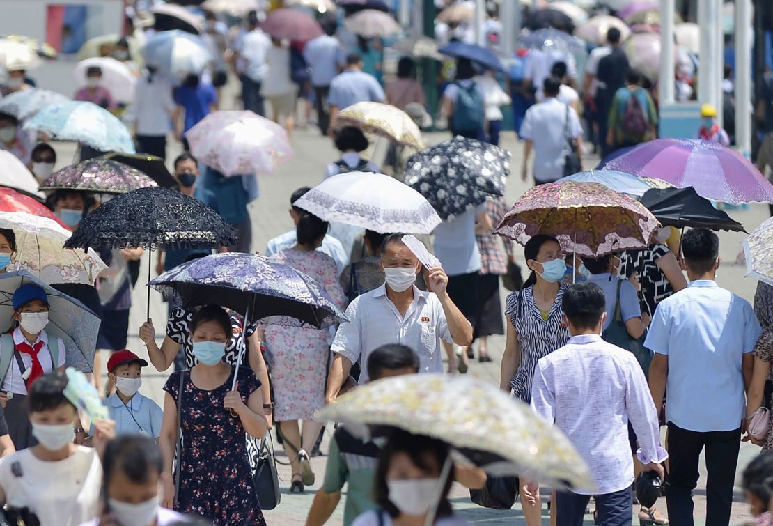 People wearing masks for protection against the coronavirus walk in Pyongyang amid the scorching summer heat on July 20, 2021.